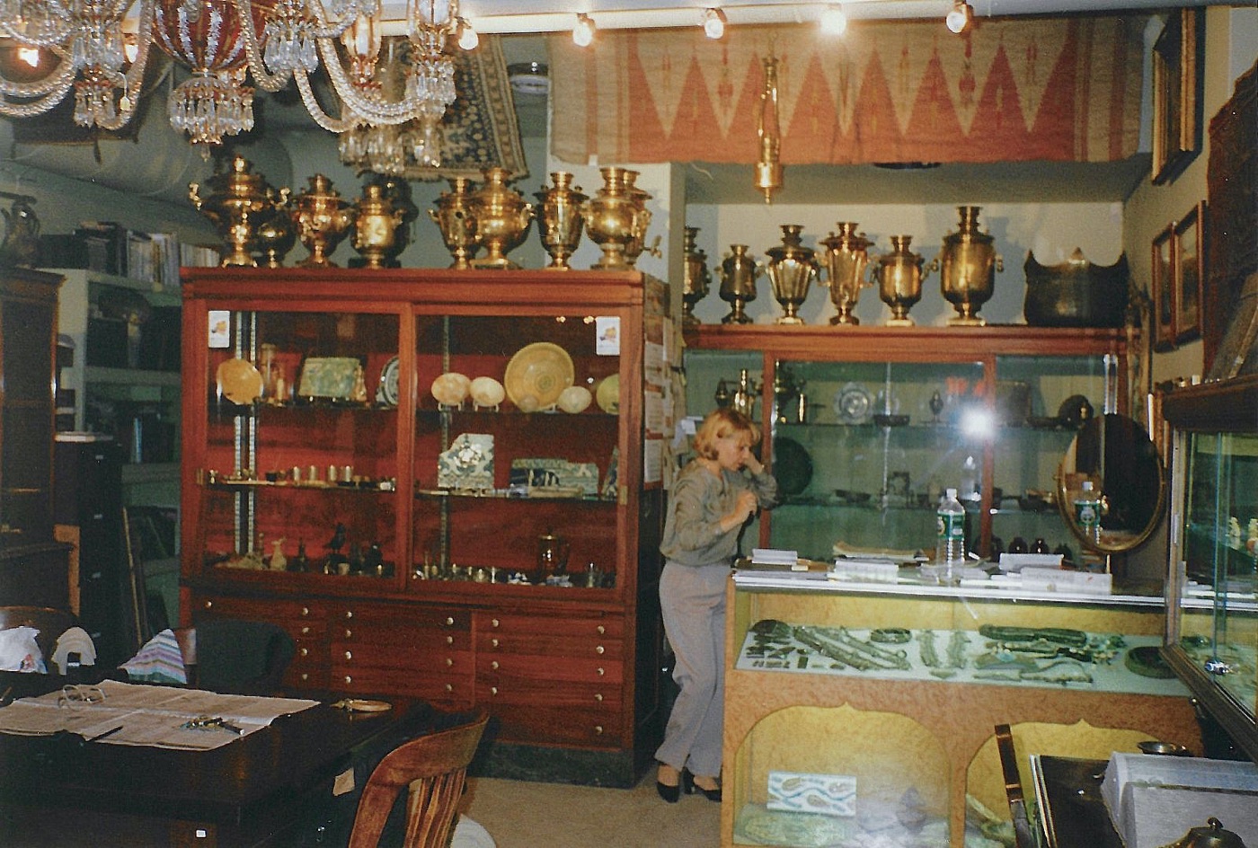 The gallery interior: two ranks of polished brass Russian samovars along the tops of the cabinets, crystal chandeliers overhead, a kilim hung on the wall, and glass cases of hardstone and metalwork below.