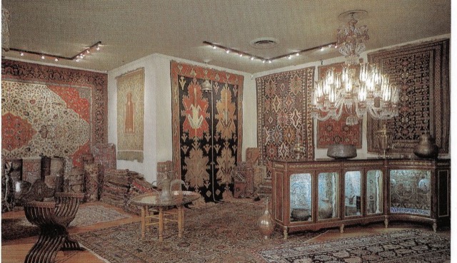 The gallery photographed for the advertisement: carpets hung on every wall under a crystal chandelier, and a curved vitrine.