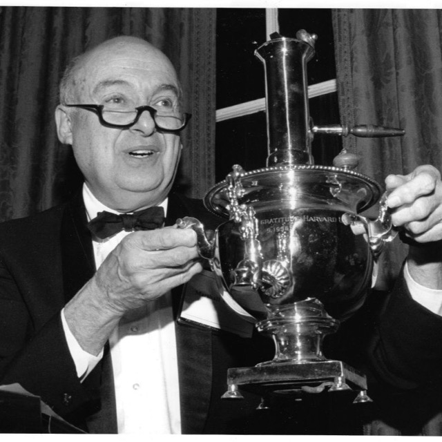A man in a dinner jacket holding up a large silver samovar engraved in gratitude to Harvard.