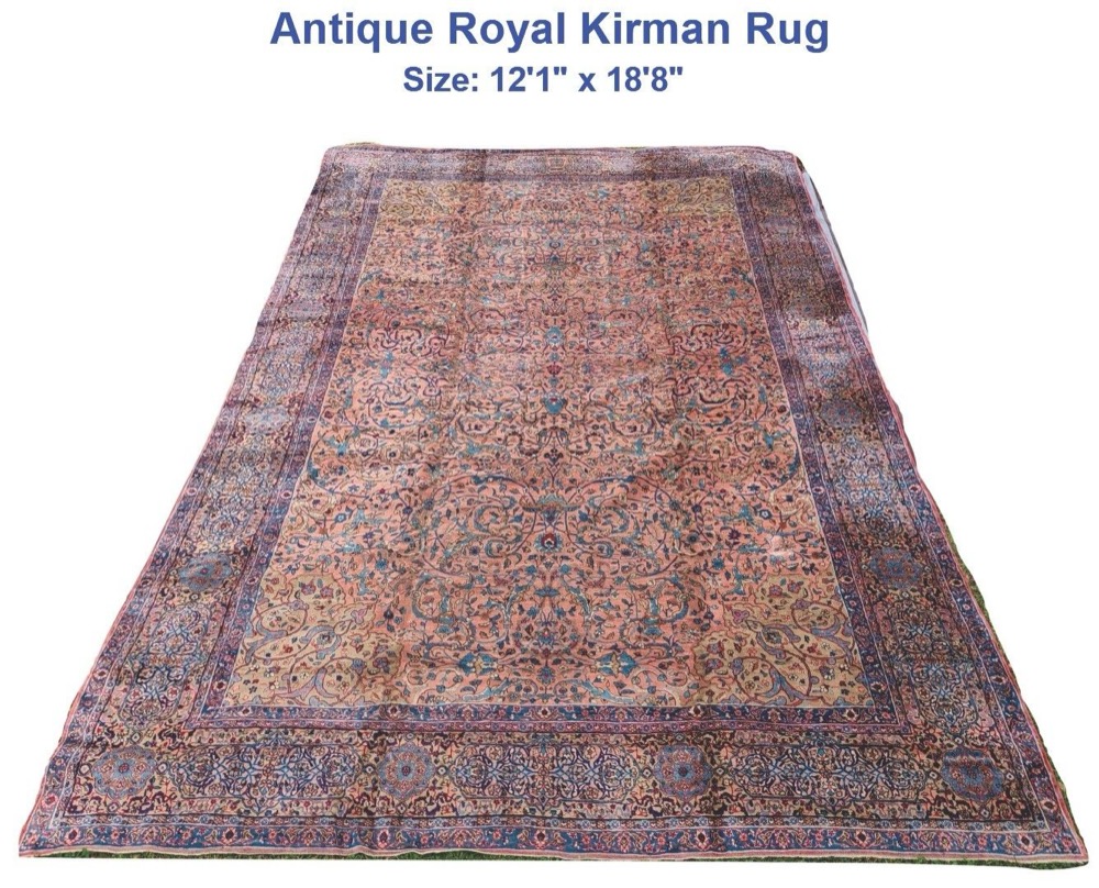 A very large antique Kirman carpet laid out flat: a soft rose field covered in flowering vines and palmettes in blue, ivory and green, inside a deep indigo border of linked floral medallions.