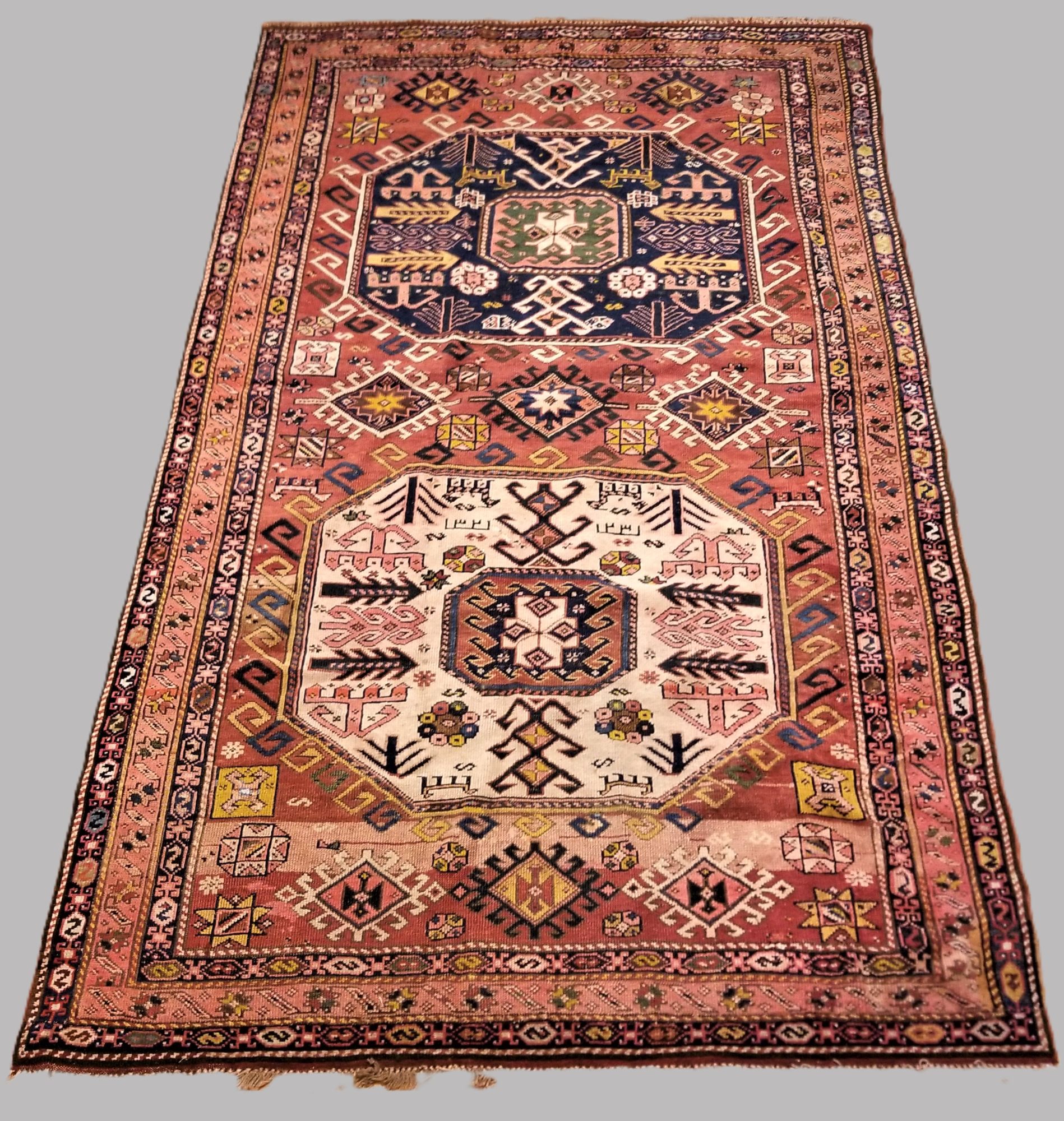 Full view of a Caucasian Kazak rug with two octagonal medallions in indigo and ivory on a rose-madder field
